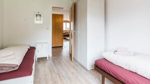 Hotellihuone, jossa on kaksi sänkyä, vaatekaappi, yöpöytä ja ovi, joka johtaa kylpyhuoneeseen.