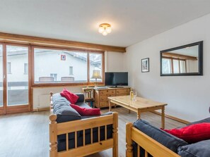 Un salon meublé comprenant un canapé, une table en bois, un téléviseur et une grande fenêtre.