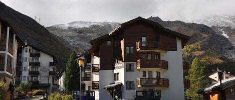 A multi-story hotel with balconies, a paved pathway, and a mountain backdrop.