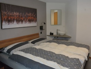 A bedroom with a large bed, a bedside table, a wall-mounted lamp, and a painting. - Achat Appartement/Fewo 4-Bettwohnung Nr. 1 by Interhome (Saas-Fee)