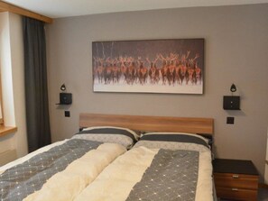 A bedroom with a bed, a headboard, a wall-mounted painting, bedside tables, and a window with curtains. - Achat Appartement/Fewo 4-Bettwohnung Nr. 1 by Interhome (Saas-Fee)