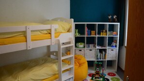 Et børneværelse med køjesenge, en bogreol og et legetæppe.