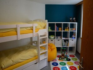 Ein Kinderzimmer mit Etagenbetten, einem Bücherregal und einer Spielmatte.