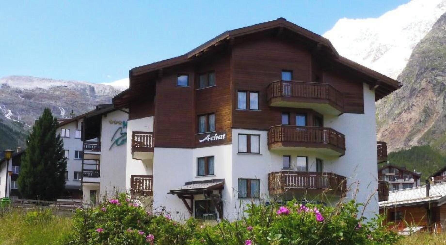 Ein mehrstöckiges Hotel mit Balkonen, im Hintergrund Berge und ein Schild, das es als Restaurant kennzeichnet.