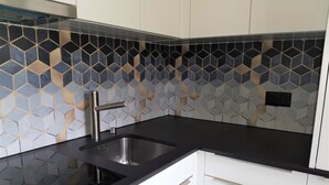 Et køkken med en sort bordplade, en rustfri stålvask og et bagpanel med et geometrisk flisemønster.