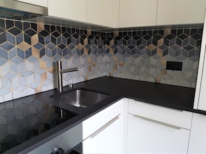 Eine Küche mit schwarzem Arbeitsplatz, einer Edelstahl-Spüle und einer Rückwand mit einem geometrischen Fliesenspiegel.