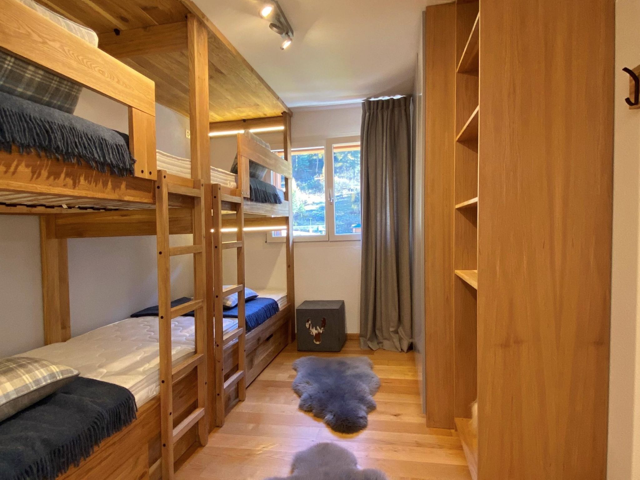 A room with bunk beds, a small rug, a cabinet, and a window with curtains.