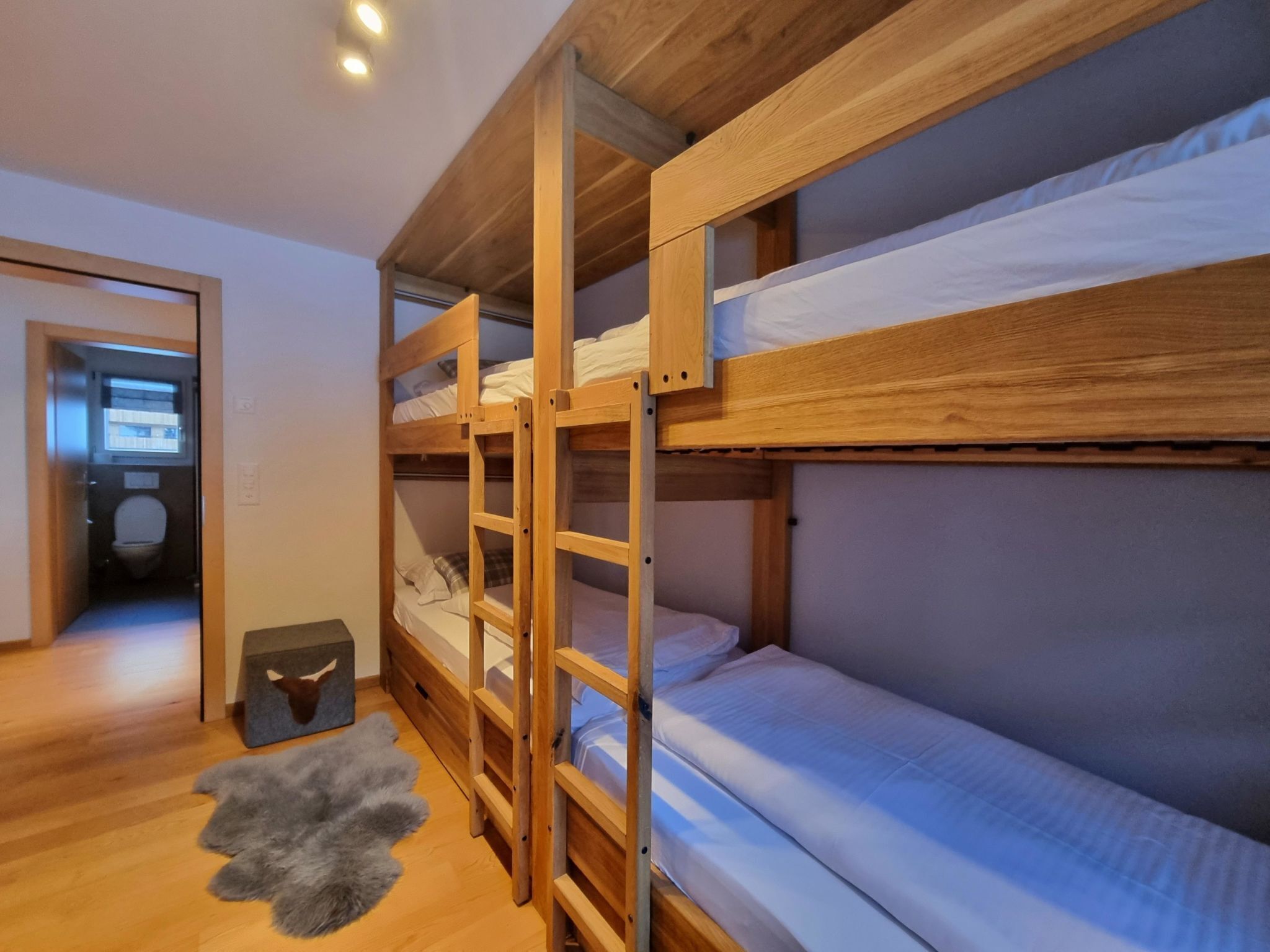 Una camera con letto a castello, pavimento in legno, tappeto in pelliccia grigia e porta che dà su un bagno.