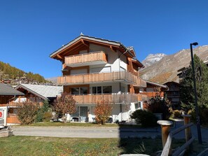 Ein mehrstöckiges Gebäude mit hölzernen Balkonen, einer Garage und einem Berg im Hintergrund.