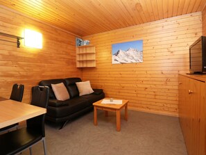 A cozy room with a wooden interior, a black leather sofa, a small wooden table, and a television on a wooden cabinet. - Chalet Ideal Appartement/Fewo 3-Bettwohnung Nr. 4 by Interhome (Saas-Fee)