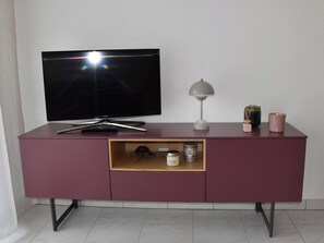 Ein Flachbildfernseher an einer Wand über einem bordeauxroten Schrank mit einer Ablage darunter.
