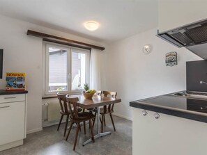 Een kleine keuken met een eettafel, stoelen, een fornuis en een raam met uitzicht.