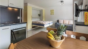 A compact kitchen with a stove and oven, a bed with a mattress and pillows, a sofa, and a small table with a fruit bowl. - Alouette Appartement/Fewo 2-Bettwohnung Nr. 17 by Interhome (Saas-Fee)