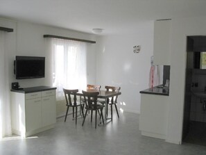 Eine kompakte Küche mit Essbereich, einem flachbildfernseher an der Wand und einem kleinen Kühlschrank.