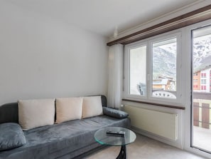 A living room with a grey sofa, a glass coffee table, and a large window with a view of buildings and mountains. - Alouette Appartement/Fewo 2-Bettwohnung Nr. 17 by Interhome (Saas-Fee)