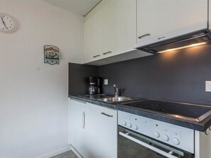 A compact kitchen with white cabinets, a black countertop, a stove with controls, and a coffee maker. - Alouette Appartement/Fewo 2-Bettwohnung Nr. 17 by Interhome (Saas-Fee)