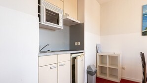 A compact kitchen with a microwave, sink, and a small refrigerator. There is a white cabinet with a shelf, a trash bin, and a white shelving unit. - Classic Riviera Escape with Pool, Grasse (Grasse)