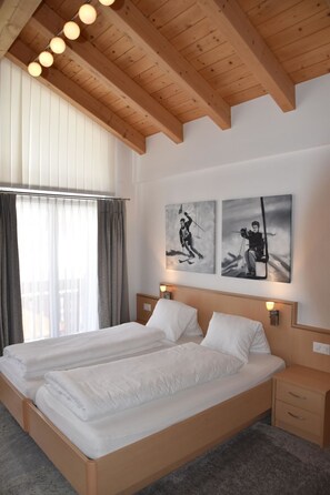 Habitación de hotel con techo de madera, una cama grande con ropa blanca, dos mesitas de noche y una obra de arte en la pared.