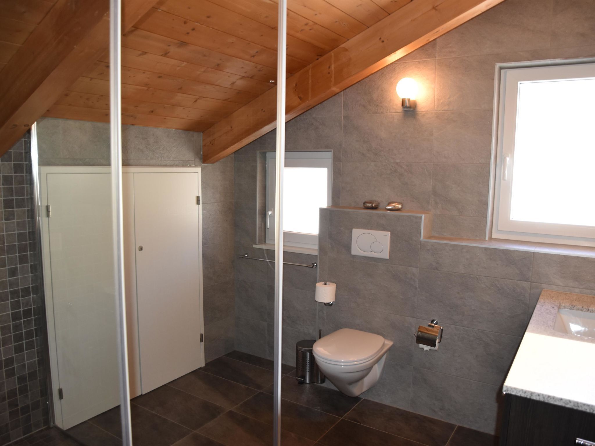 Bagno con doccia, toilette e lavandino, con soffitto in legno e pareti rivestite di piastrelle.