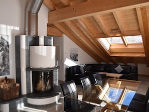A modern living room with a fireplace, a glass dining table, and a black leather sofa. - Cornelia 25 Appartement/Fewo 6-Bettwohnung Nr. 25 by Interhome (Saas-Fee)