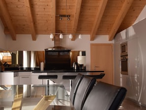 A modern kitchen with wooden beams, a central island, stainless steel appliances, and a glass dining table. - Cornelia 25 Appartement/Fewo 6-Bettwohnung Nr. 25 by Interhome (Saas-Fee)