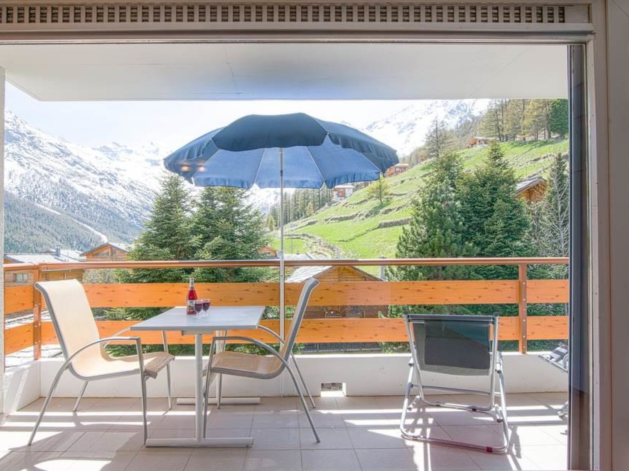 A balcony with a table and chairs, a bottle of wine, and a view of a mountain landscape.