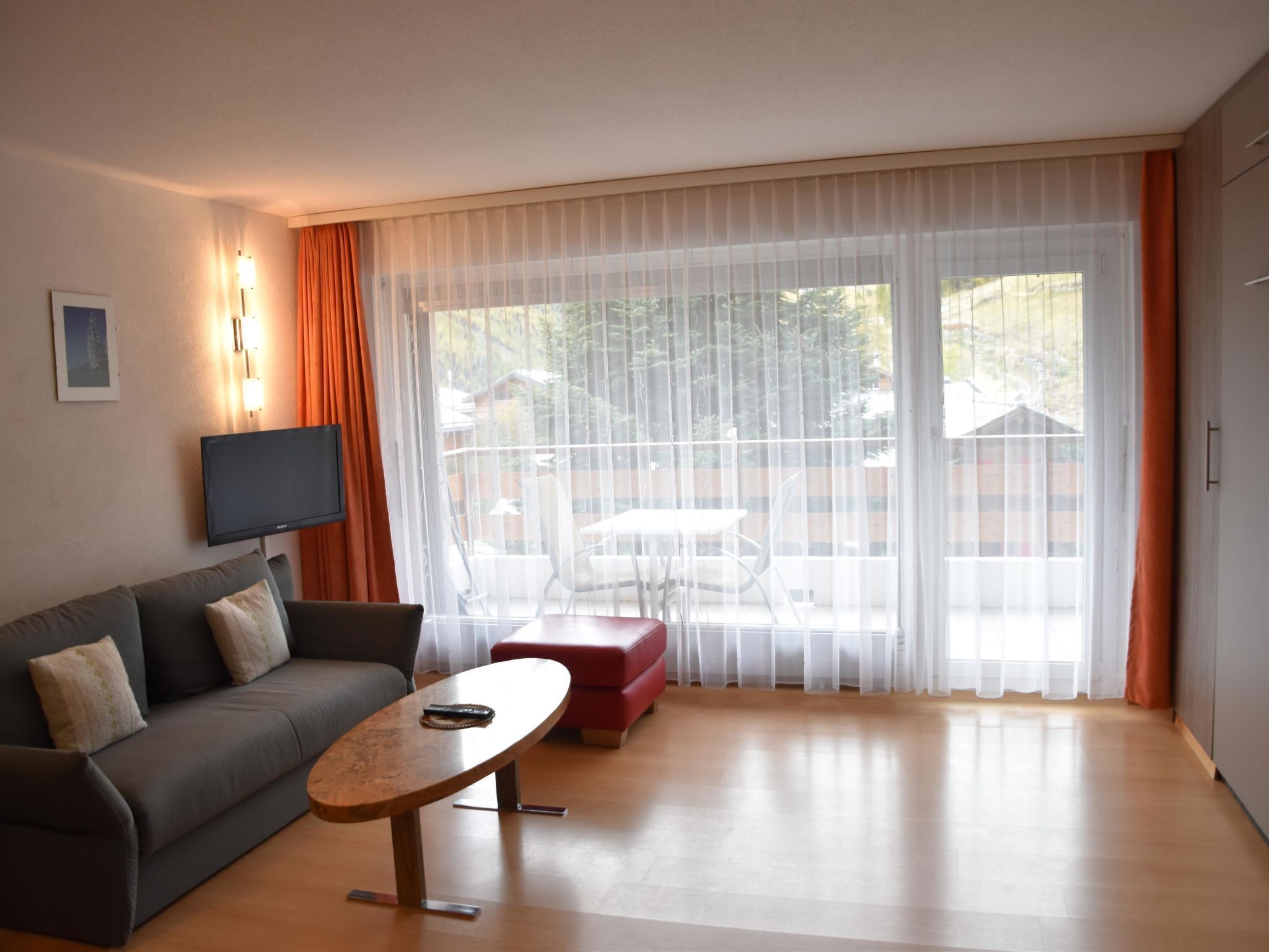Ein modernes Wohnzimmer mit Sofa, Couchtisch, Fernseher und einer Schiebetür zu einem Außenbereich.