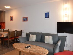 Un salon comprenant un canapé, une table basse, un téléviseur fixé au mur et un coin repas avec des chaises et une table.