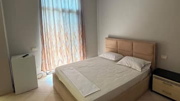 Un dormitorio con cama, mesita de noche, un pequeño armario blanco y un equipo de aire acondicionado.