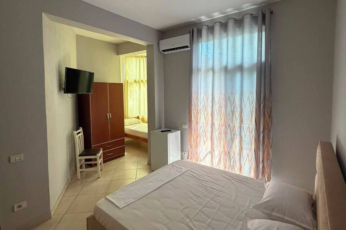 A bedroom with a bed, a TV, an air conditioning unit, and a window with curtains.