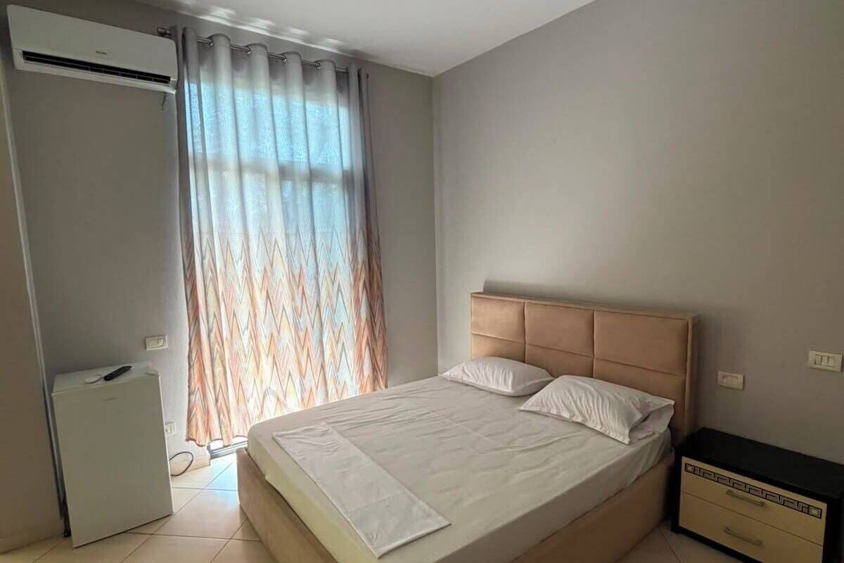 A bedroom with a bed, a nightstand, an air conditioning unit, and a window with curtains.