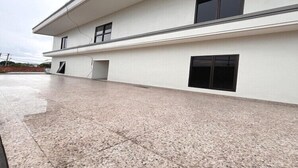 Un edificio moderno con techo plano, ventanas amplias y un amplio espacio pavimentado en la parte frontal.