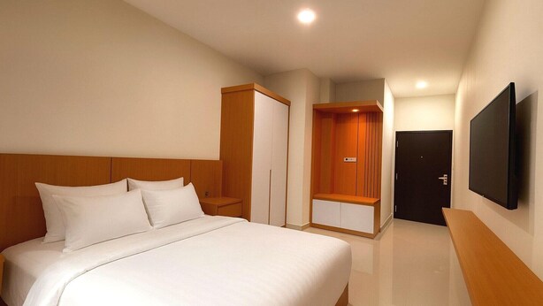 Habitación de hotel con una cama grande, un armario, un banco y un televisor montado en la pared.