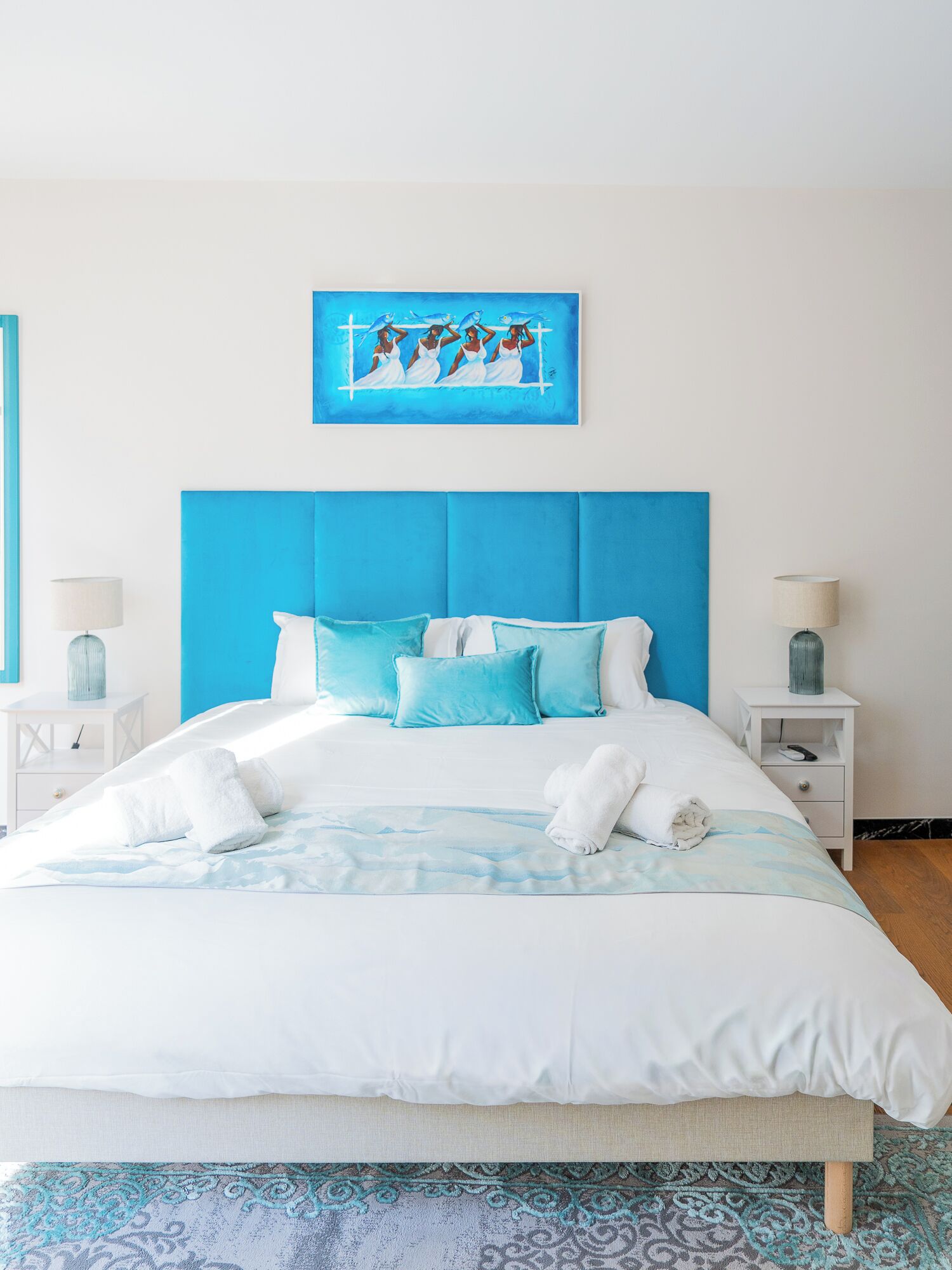 A bed with a blue headboard, white bedding, and a blue-patterned throw.