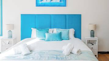 A bed with a blue headboard, white bedding, and a blue-patterned throw.