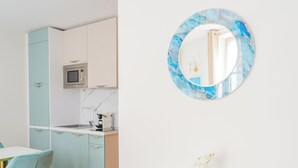 Una cocina moderna con microondas, lavamanos y armarios, un espejo redondo con diseño de mármol azul, y un aparador blanco con un jarrón de flores.