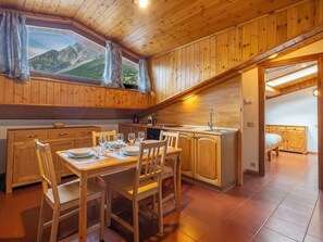A wooden interior with a dining area, kitchen, and a bedroom with a window view. - Condominio Europa N27 by Interhome (Bormio)