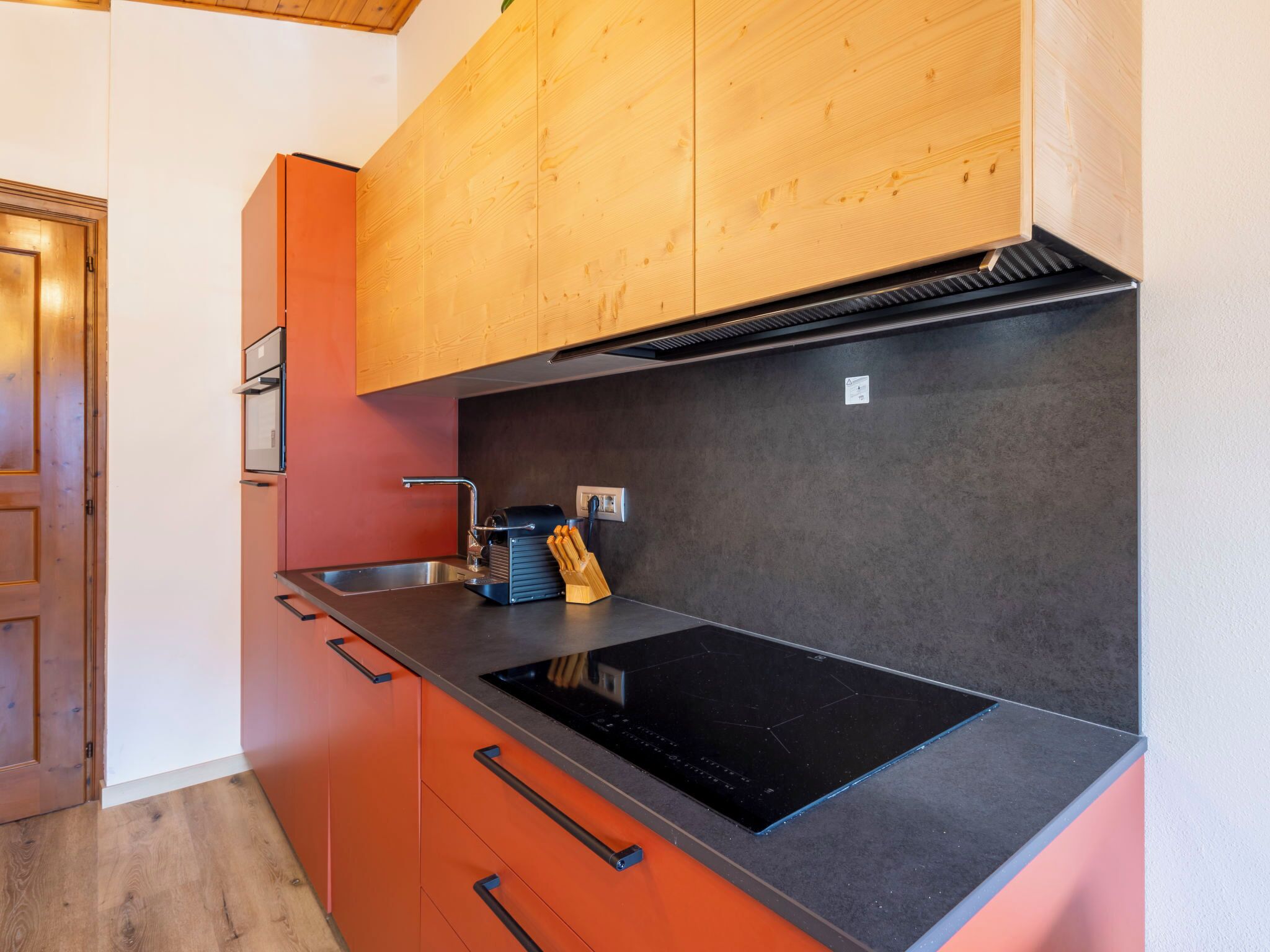 Eine moderne Küche mit Holzausstattung, einer schwarzen Induktionskochplatte und einem Edelstahl-Spülbecken.