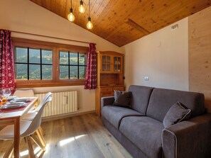 A cozy room with a wooden ceiling, a grey sofa, a dining table with chairs, and a window with curtains. - Condominio Europa N26 by Interhome (Bormio)