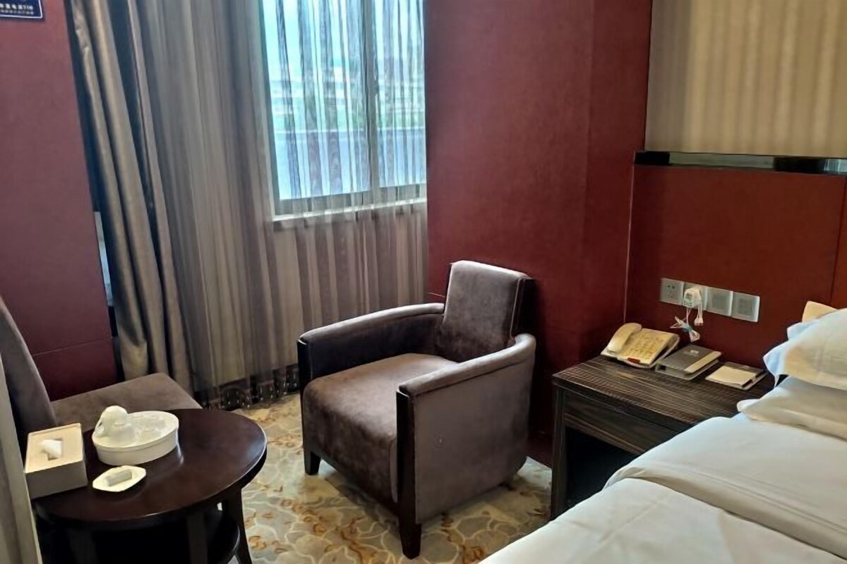 A hotel room with a single bed, a chair, a small table with a phone, and a window with curtains.