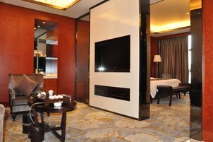 Una habitación de hotel con televisión, cama, escritorio con silla y zona de comedor.