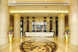 Zona de recepción de un hotel con mostrador de mármol, amplias columnas, relojes y un diseño decorativo en el suelo.
