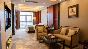 A hotel room with a bed, a sofa, a coffee table, a TV, and a large window.