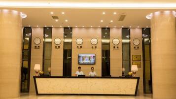 A hotel reception area with a marble counter, two receptionists, and a television screen.