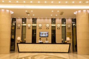 A hotel reception area with a marble counter, two receptionists, and a television screen. - DINGMEIHUI Holiday Hotel (Zhangpu)