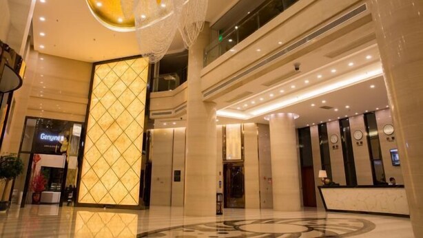 A modern hotel lobby with a reception desk, elevators, and a large illuminated wall.