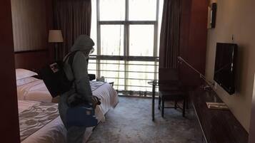 A hotel room with a bed, a desk, a chair, a television, and a large window.