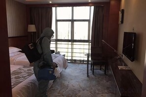 Habitación de hotel con cama, escritorio, silla, televisor y un amplio ventanal.