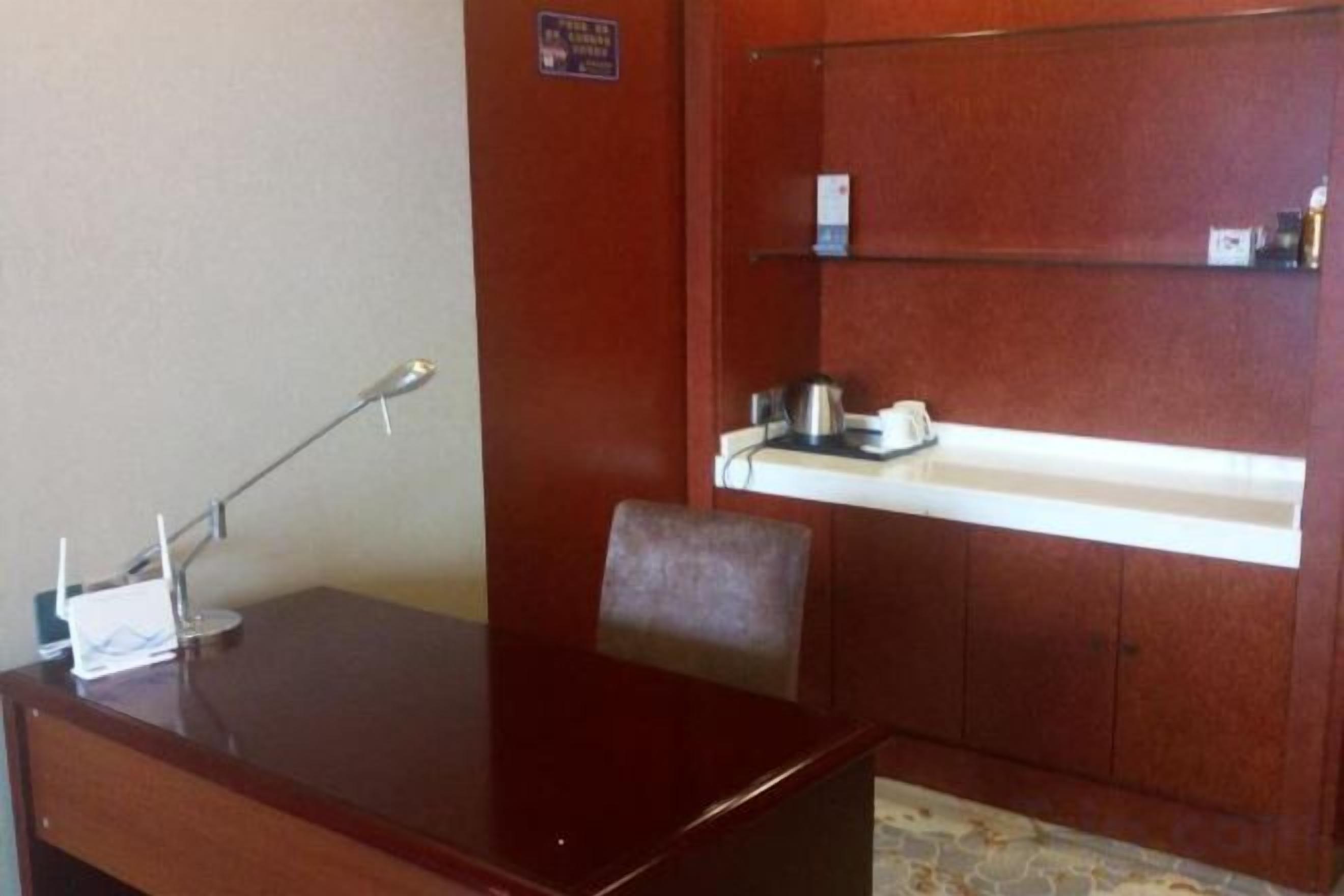 A room with a wooden desk, a chair, a shelf with a kettle, and a small cabinet.