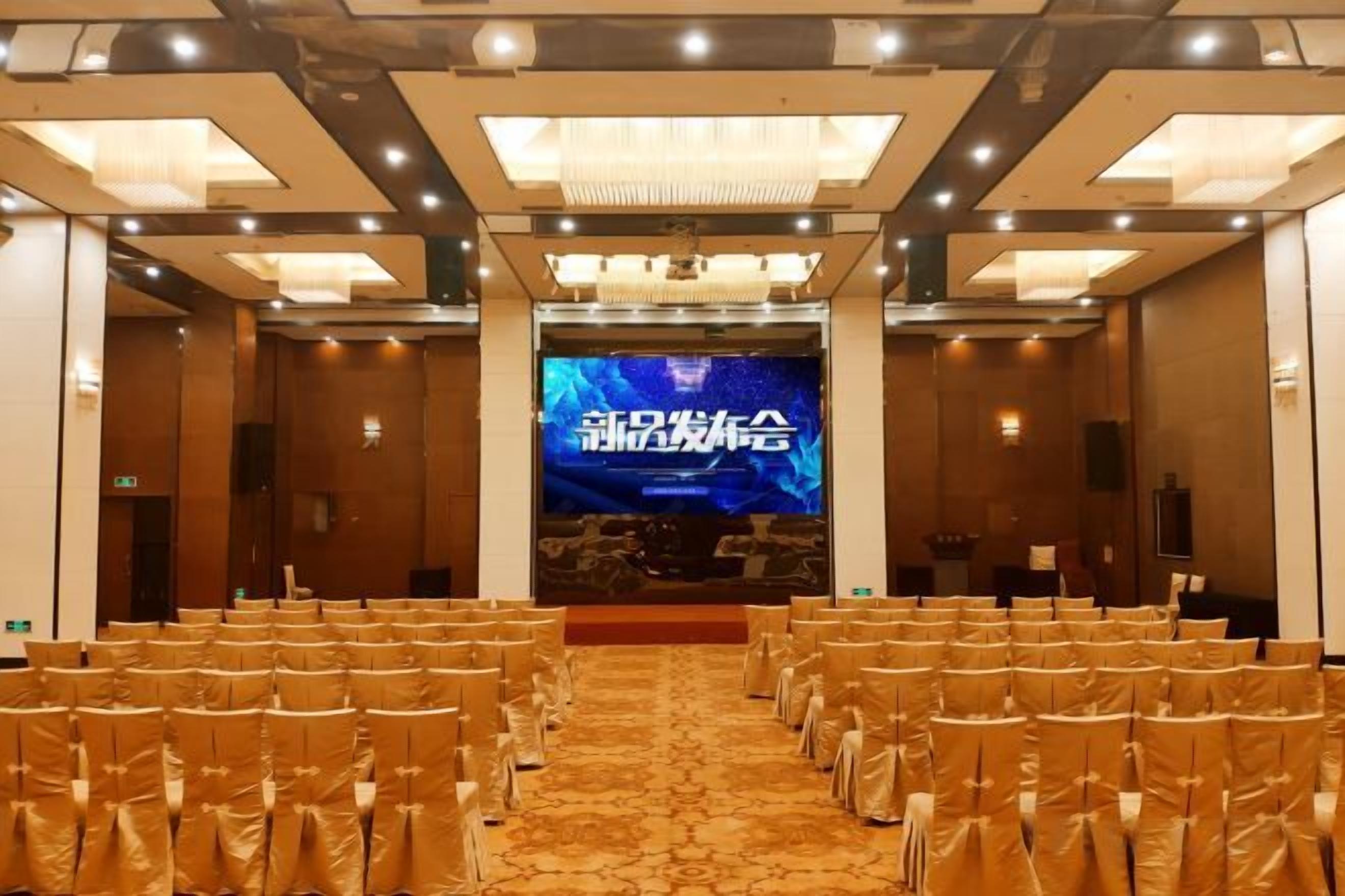 A conference room with rows of chairs, a large screen at the front, and a carpeted floor.